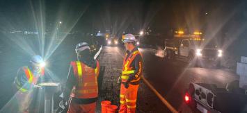 Three WSDOT workers in full safety gear working in work zone at night.